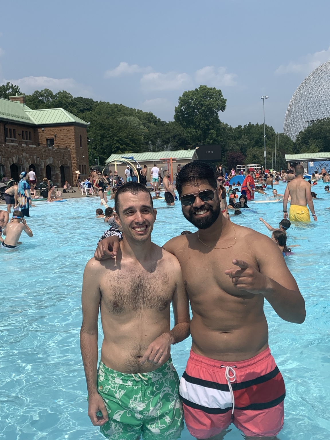Two buddies smiling together beside an outdoor swimming pool